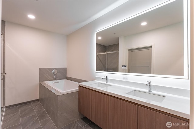 bathroom with recessed lighting, a garden tub, a sink, and double vanity