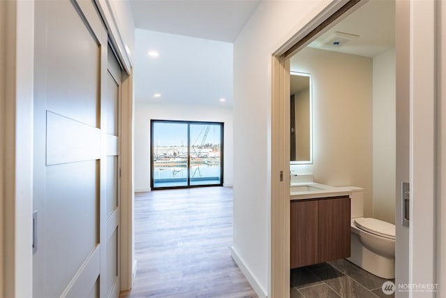 hall featuring a sink, baseboards, wood finished floors, and recessed lighting