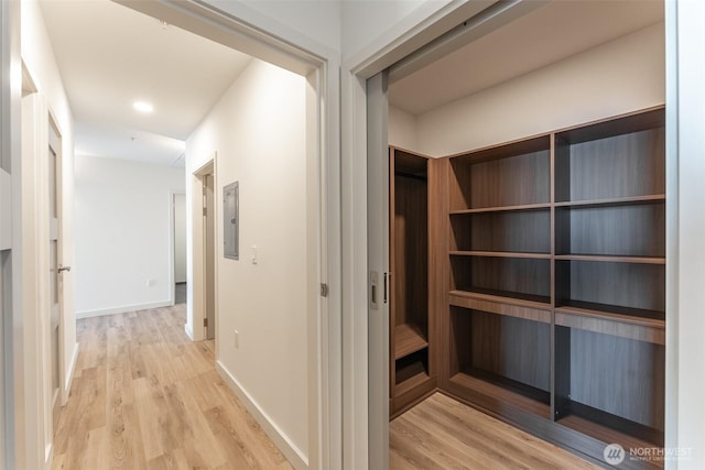 hallway featuring electric panel, baseboards, and light wood finished floors