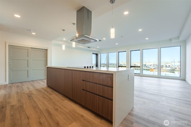 kitchen with island range hood, a water view, light countertops, brown cabinetry, and an island with sink