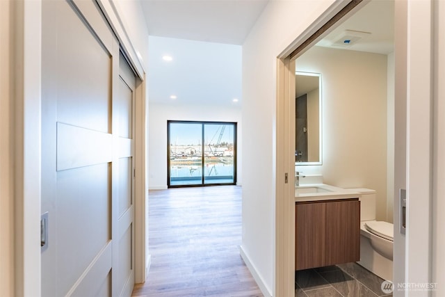 corridor with recessed lighting, baseboards, a sink, and wood finished floors