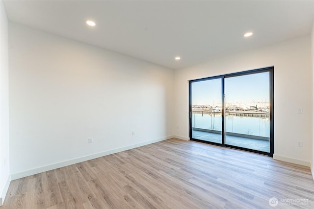 empty room with light wood-type flooring, a water view, baseboards, and recessed lighting