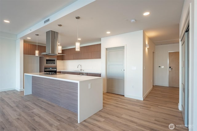 kitchen with island range hood, modern cabinets, appliances with stainless steel finishes, hanging light fixtures, and light countertops