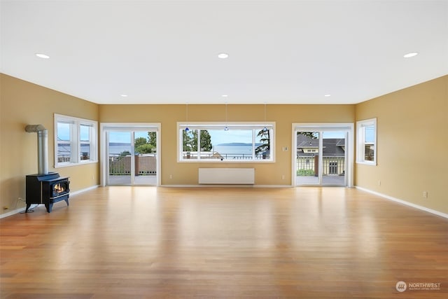 unfurnished living room with light wood-type flooring, a wood stove, and radiator heating unit