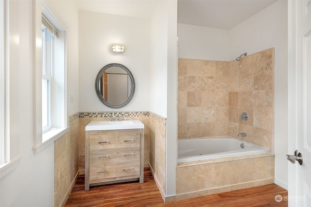 bathroom featuring tile walls, tiled shower / bath, vanity, and wood-type flooring