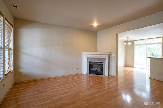 unfurnished living room with visible vents, a tiled fireplace, an inviting chandelier, light wood-type flooring, and baseboards