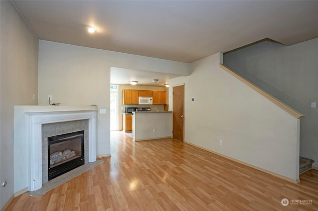 unfurnished living room featuring light wood-type flooring, stairway, and a tiled fireplace