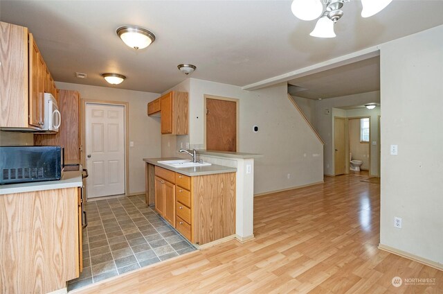 kitchen featuring light countertops, a sink, light wood-style flooring, and white microwave