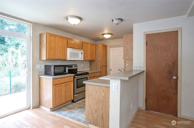 kitchen with electric stove, light countertops, white microwave, a sink, and a peninsula