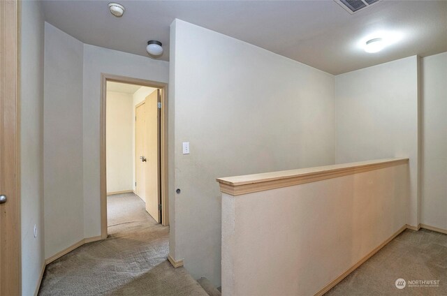 corridor featuring carpet floors, baseboards, visible vents, and an upstairs landing