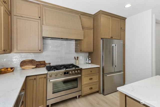 kitchen with appliances with stainless steel finishes, decorative backsplash, light wood-style flooring, and custom range hood