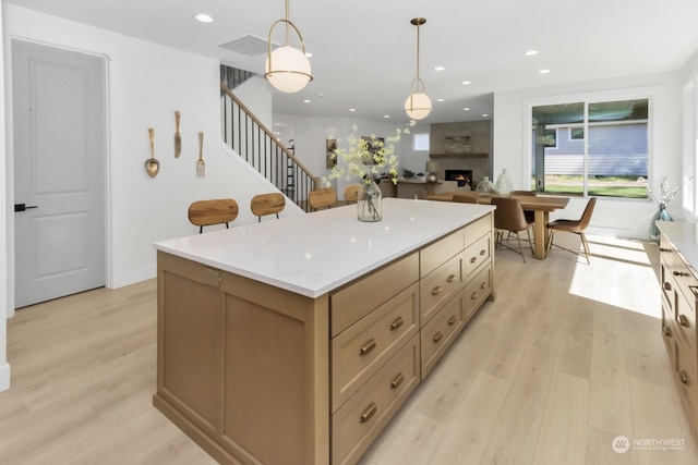 kitchen with light wood-style floors, a center island, a large fireplace, and decorative light fixtures