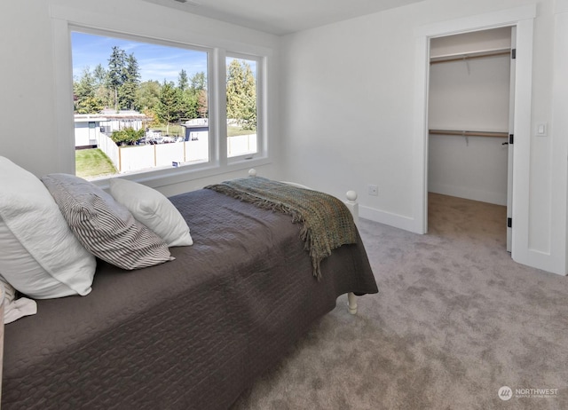 carpeted bedroom with a walk in closet and baseboards