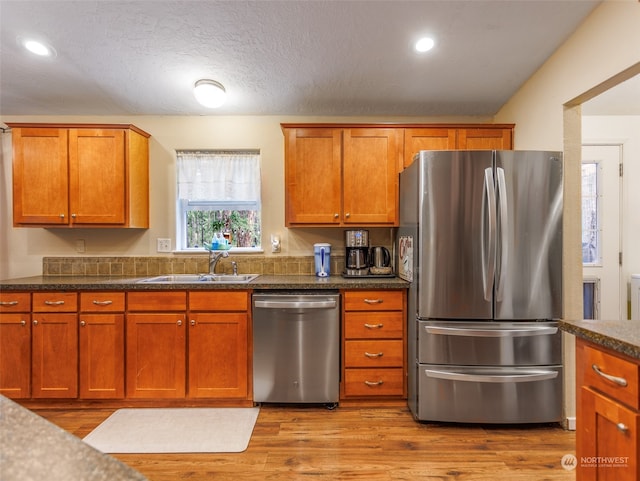 kitchen with a textured ceiling, dark stone countertops, light wood-type flooring, stainless steel appliances, and sink