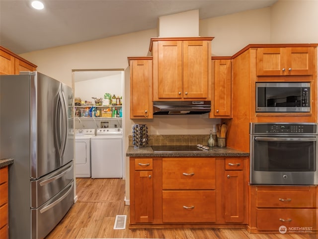 kitchen featuring dark stone counters, vaulted ceiling, light wood-type flooring, stainless steel appliances, and separate washer and dryer