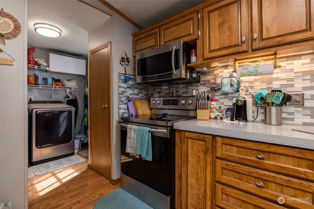 kitchen with tasteful backsplash, washer / dryer, appliances with stainless steel finishes, hardwood / wood-style flooring, and crown molding