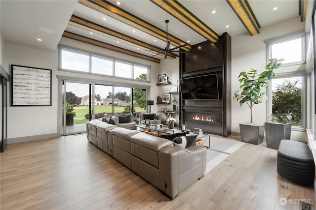 living room featuring light hardwood / wood-style floors, plenty of natural light, beamed ceiling, and a large fireplace