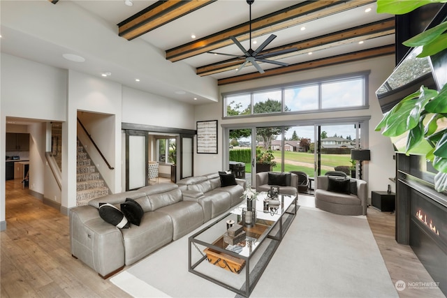 living room featuring beam ceiling, light hardwood / wood-style flooring, ceiling fan, and a towering ceiling