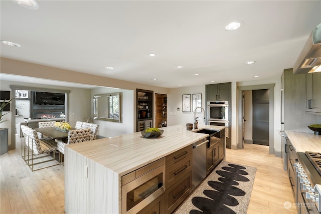 kitchen with a center island with sink, stainless steel appliances, light hardwood / wood-style floors, wood counters, and sink