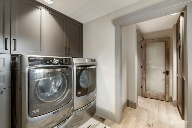 clothes washing area featuring cabinets, washing machine and clothes dryer, and light hardwood / wood-style floors