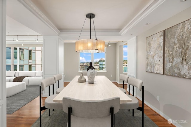 dining room with crown molding, a raised ceiling, wood finished floors, and baseboards