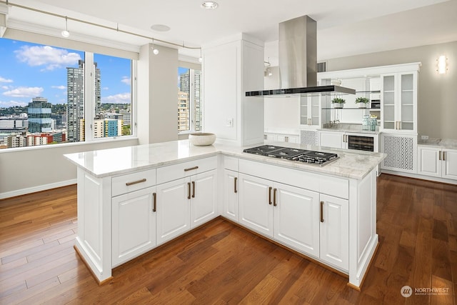 kitchen with a view of city, island range hood, stainless steel gas cooktop, white cabinetry, and dark wood-style floors