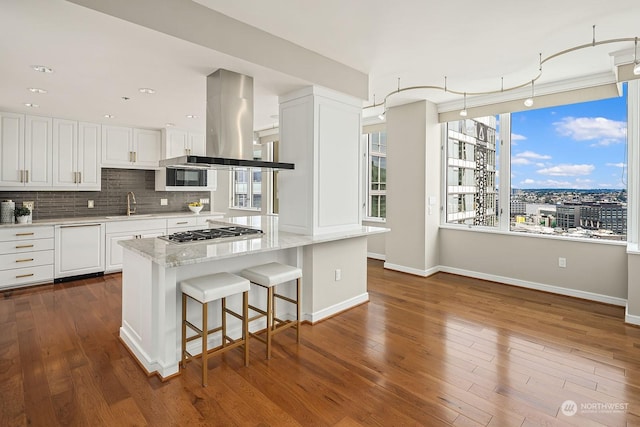 kitchen featuring light stone counters, stainless steel gas cooktop, island exhaust hood, tasteful backsplash, and white cabinets