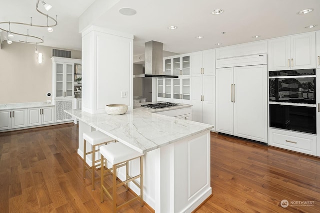 kitchen featuring white cabinets, glass insert cabinets, light stone counters, paneled built in refrigerator, and island exhaust hood