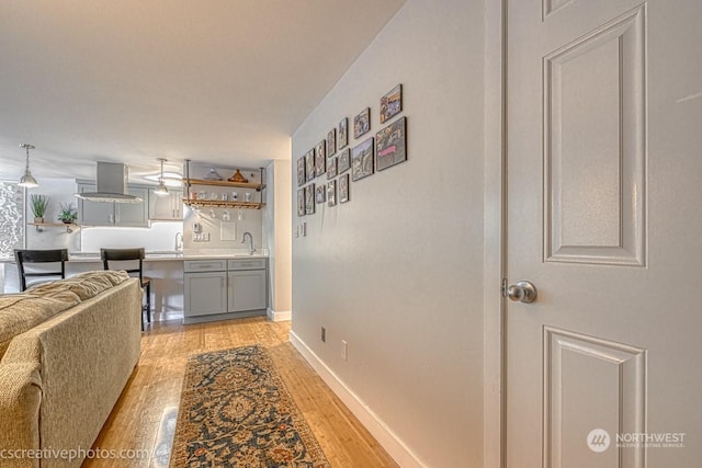 corridor featuring a sink, baseboards, and light wood-style flooring