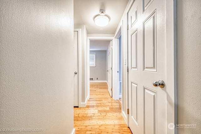 hallway featuring baseboards, light wood-style floors, and a textured wall