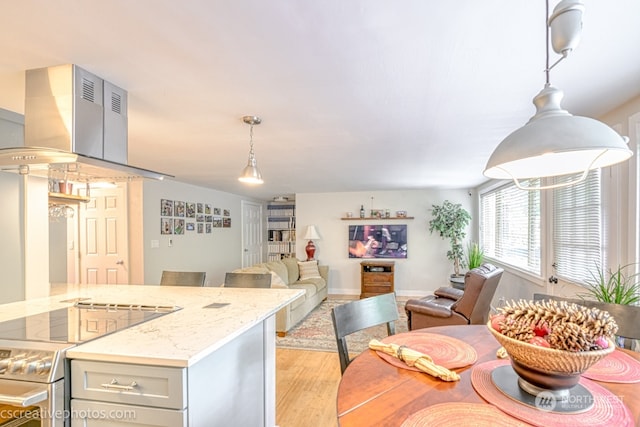 kitchen with light stone counters, light hardwood / wood-style flooring, hanging light fixtures, island exhaust hood, and electric range