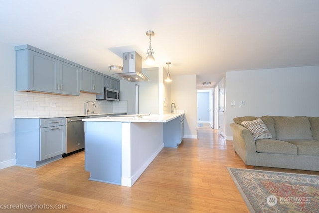 kitchen with hanging light fixtures, light hardwood / wood-style floors, island exhaust hood, decorative backsplash, and appliances with stainless steel finishes