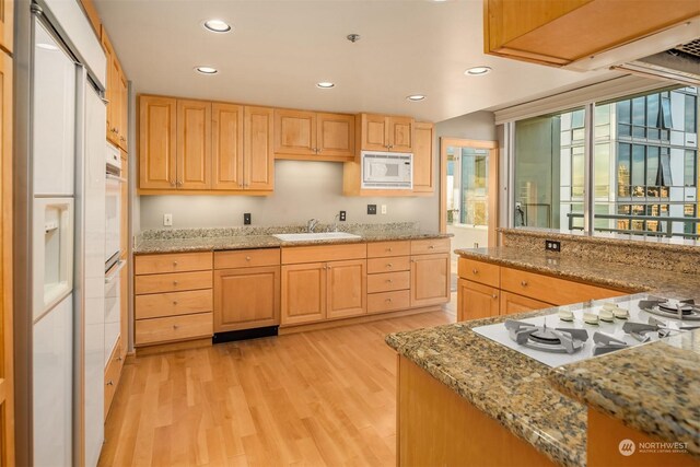 kitchen with light stone counters, white appliances, sink, light brown cabinets, and light hardwood / wood-style floors