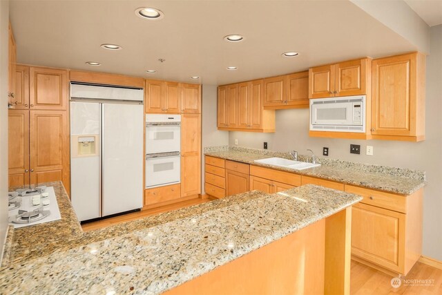 kitchen featuring light stone countertops, light wood-type flooring, sink, light brown cabinets, and built in appliances