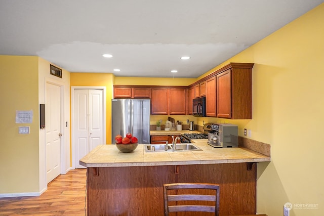 kitchen featuring appliances with stainless steel finishes, kitchen peninsula, tile countertops, light wood-type flooring, and sink