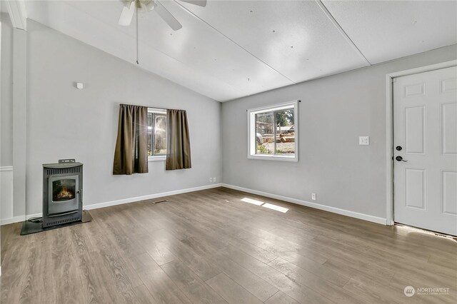 unfurnished living room featuring ceiling fan, vaulted ceiling, hardwood / wood-style flooring, and a wood stove