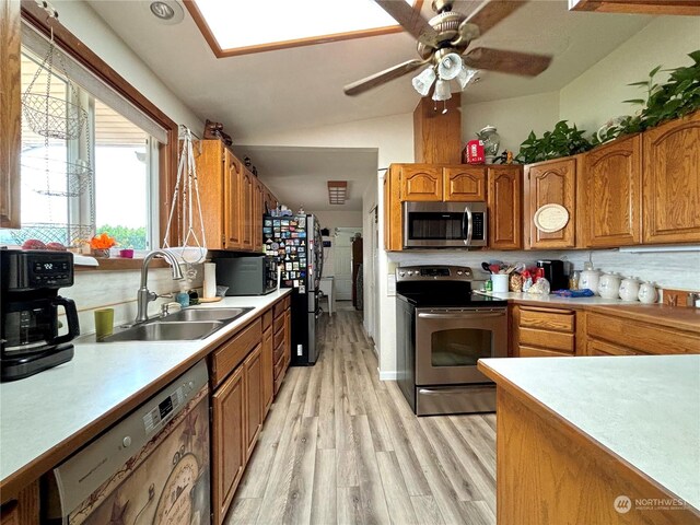 kitchen featuring appliances with stainless steel finishes, light hardwood / wood-style flooring, sink, lofted ceiling, and ceiling fan