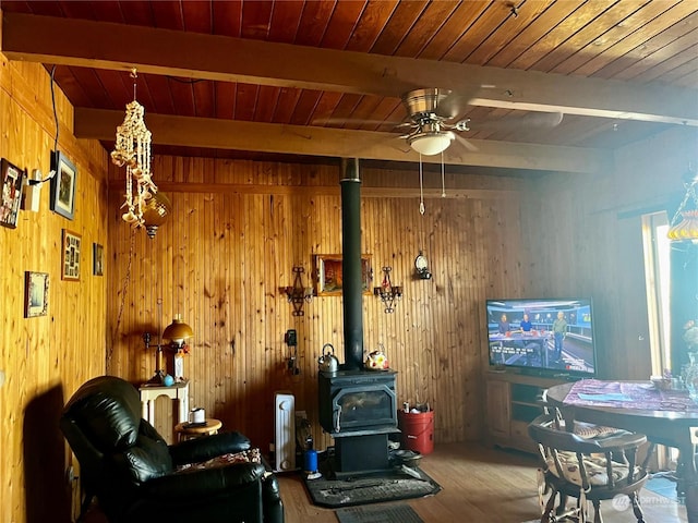 living room featuring wood ceiling, a wood stove, wood walls, ceiling fan, and beamed ceiling