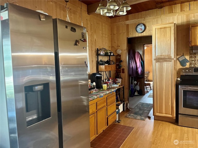 kitchen with wooden walls, light wood-style flooring, appliances with stainless steel finishes, a notable chandelier, and beam ceiling