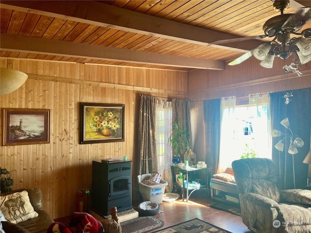 sitting room with a wood stove, wood ceiling, wooden walls, and beam ceiling