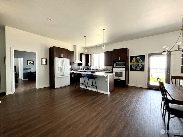 kitchen featuring a breakfast bar, dark brown cabinetry, decorative light fixtures, a kitchen island, and white appliances