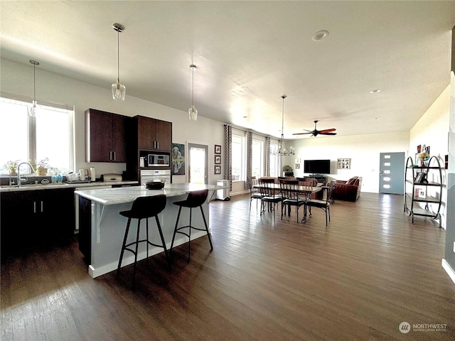 kitchen featuring a kitchen breakfast bar, dark brown cabinetry, stainless steel microwave, a kitchen island, and sink