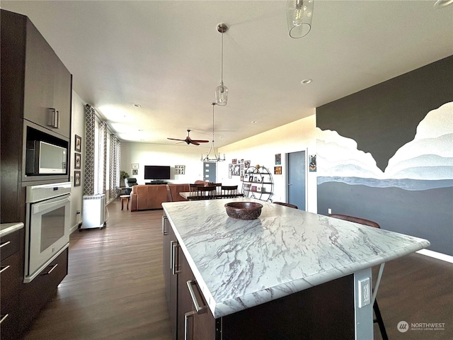 kitchen featuring dark wood-type flooring, ceiling fan, a breakfast bar, a center island, and white oven