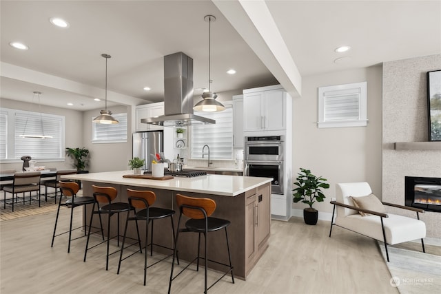 kitchen with island exhaust hood, appliances with stainless steel finishes, a spacious island, decorative light fixtures, and white cabinets