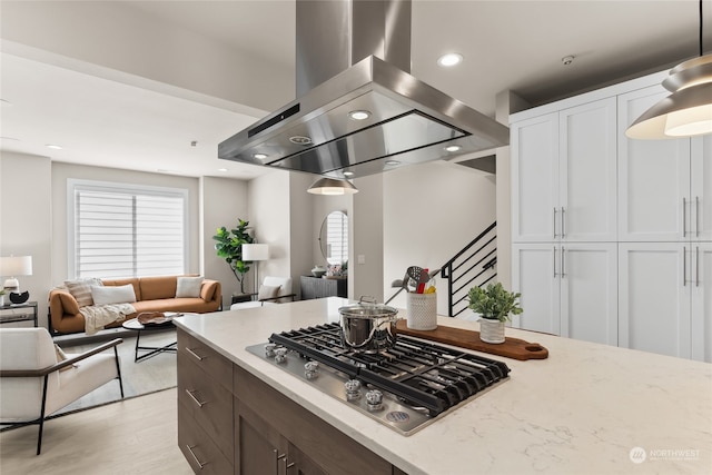 kitchen with white cabinetry, hanging light fixtures, light stone countertops, island exhaust hood, and stainless steel gas stovetop