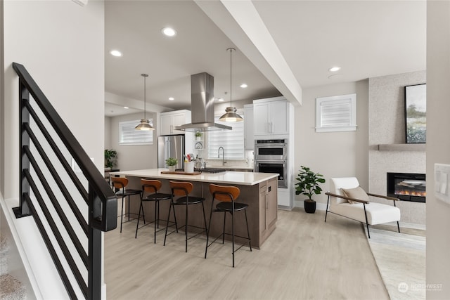 kitchen featuring a kitchen island, appliances with stainless steel finishes, pendant lighting, white cabinetry, and island exhaust hood