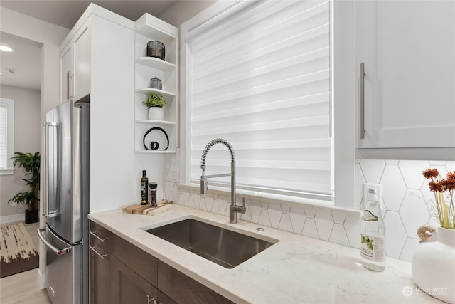 kitchen featuring white cabinetry, sink, stainless steel fridge, and light stone counters