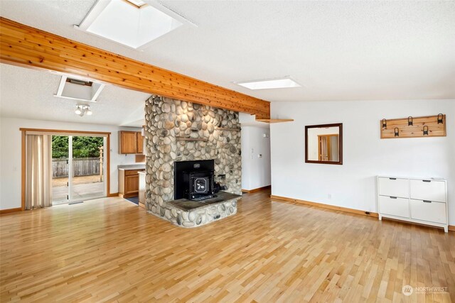 unfurnished living room featuring a textured ceiling, light hardwood / wood-style flooring, lofted ceiling with skylight, and a wood stove