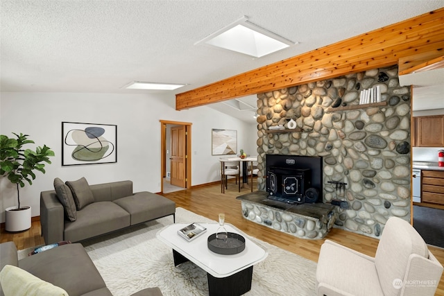 living room with light wood-type flooring, vaulted ceiling with skylight, a textured ceiling, and a wood stove