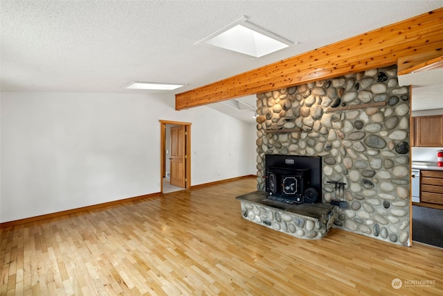 unfurnished living room featuring a textured ceiling, light wood-type flooring, lofted ceiling with skylight, and a wood stove